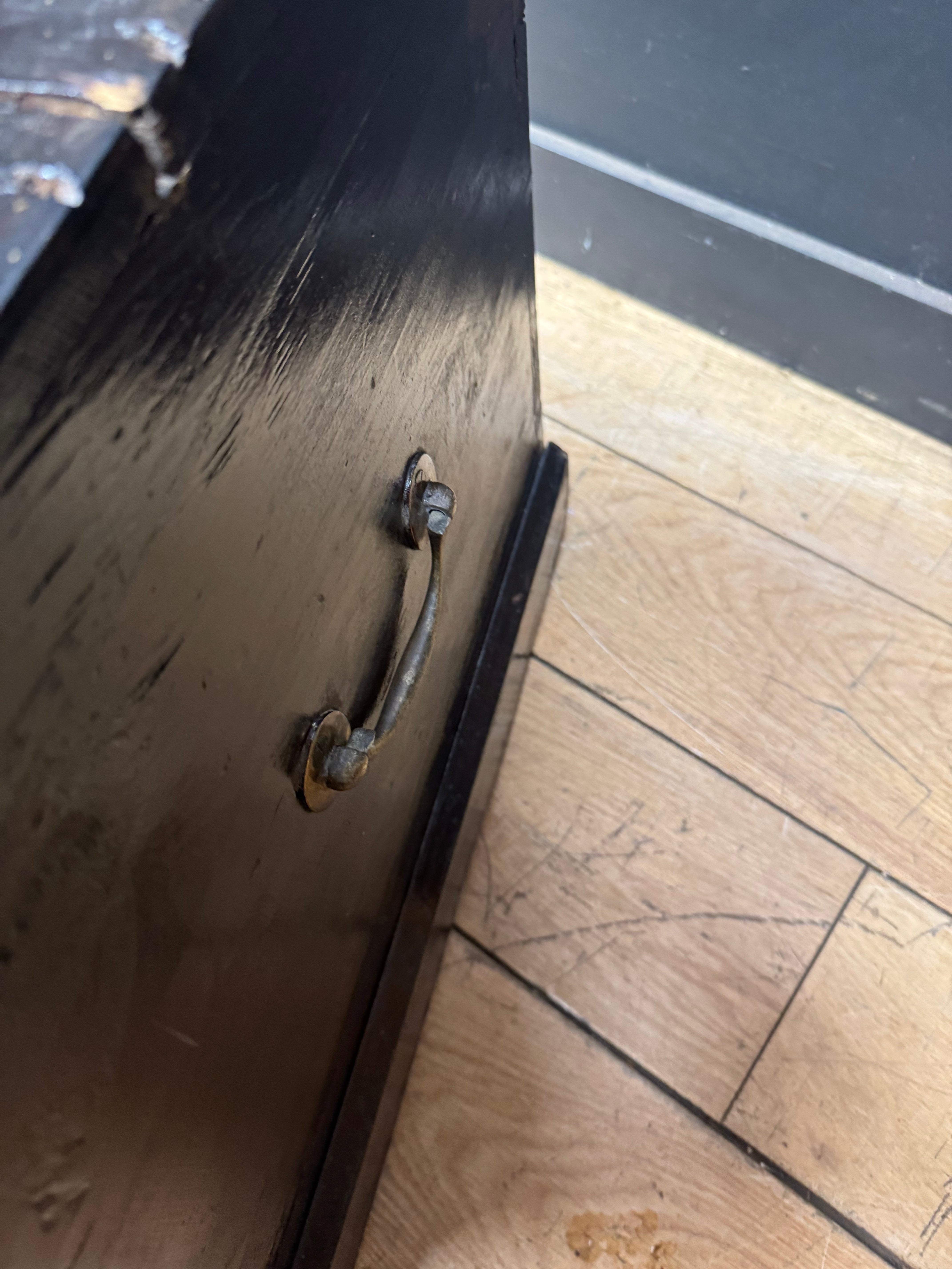 A weathered dark brown wooden drawer with rustic metal handle on an antique pine trunk coffee table storage chest