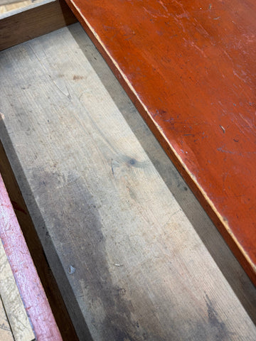 A worn light-colored pine washstand plank with visible grain and scratches sits next to a reddish-orange painted surface