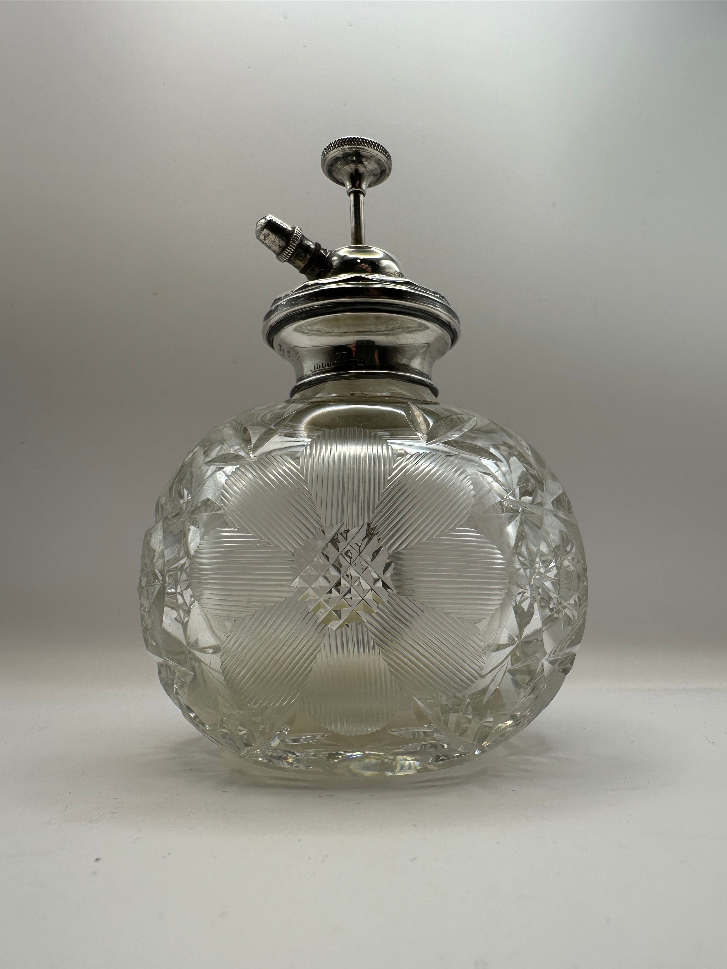 A clear cut glass perfume atomizer with an antique silver topped spray nozzle for dressing table use