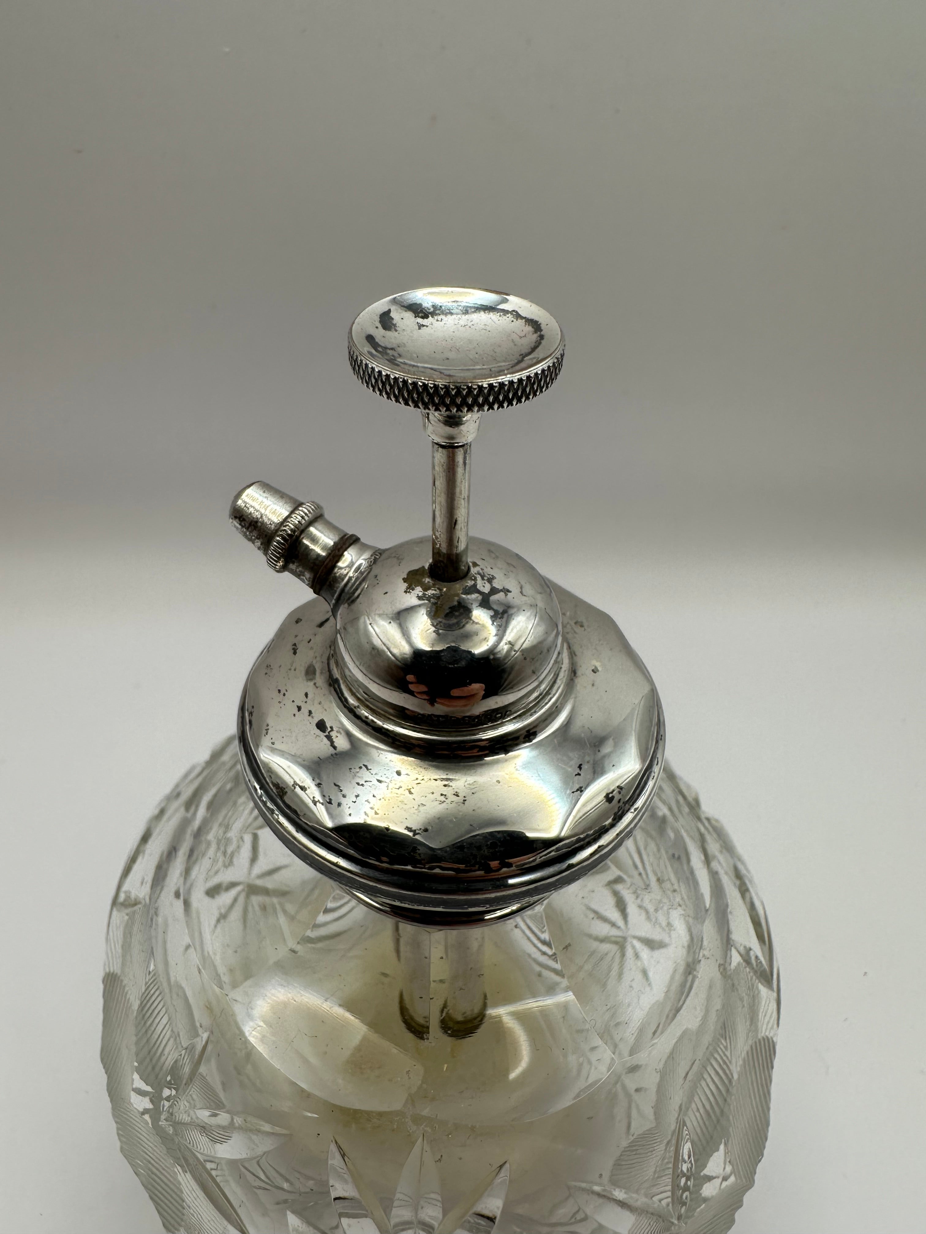 A clear cut glass perfume atomizer with an antique silver topped metal nozzle for dressing table use