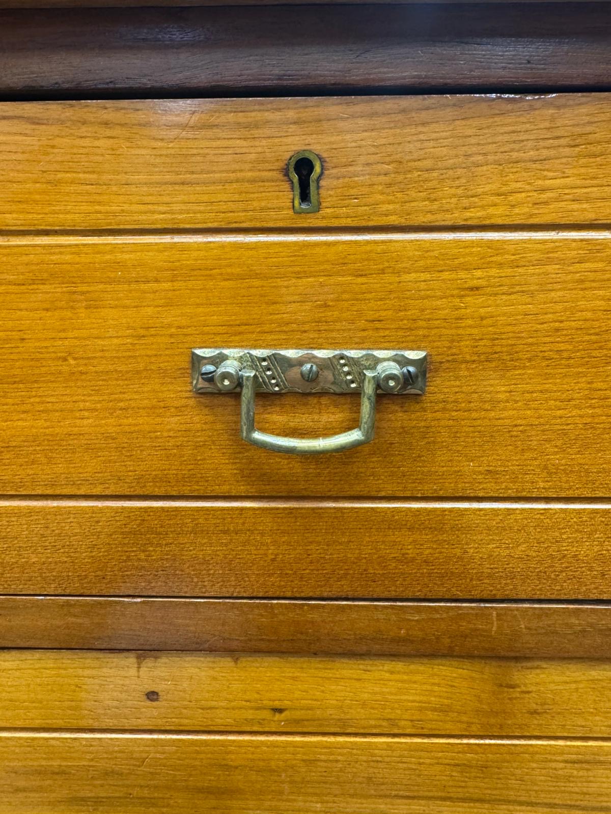 Antique walnut chest of drawers by maple and co with ornate brass drawer pulls on warm wood drawer fronts
