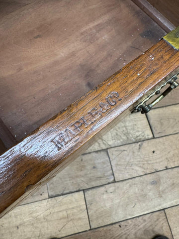 A dark brown walnut table leg with brass latch and maple & co branding on an antique drawer front