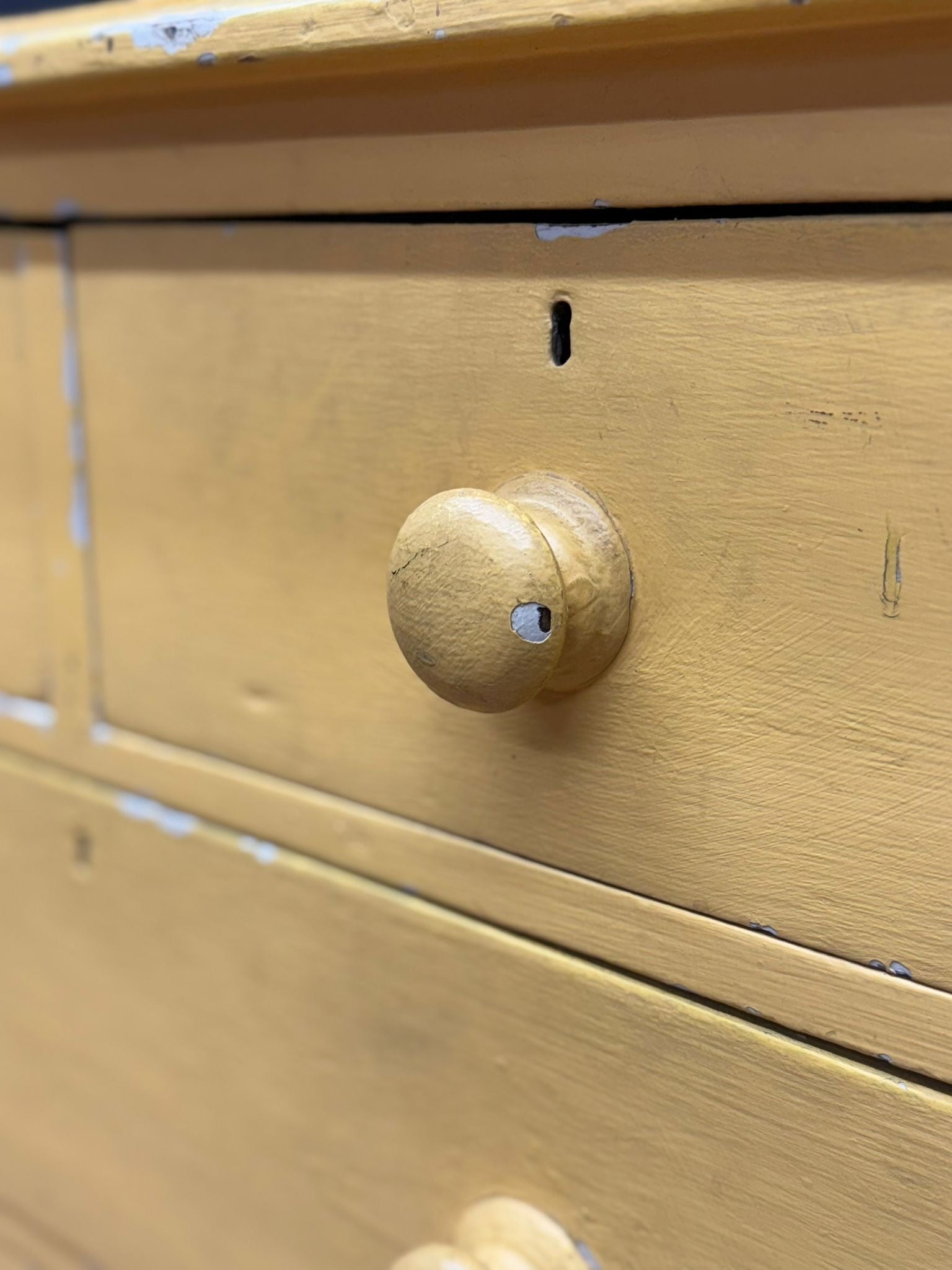 A round light-colored wooden drawer knob with worn finish on antique yellow pine chest for farmhouse bedroom storage