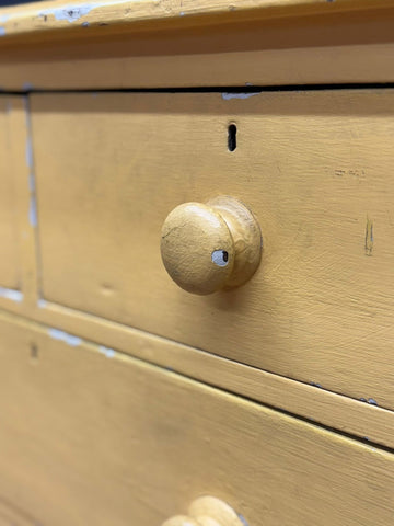 A round light-colored wooden drawer knob with worn finish on antique yellow pine chest for farmhouse bedroom storage