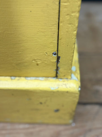 Corner of yellow painted pine chest with chipped paint and small hole ideal for bedroom storage or sink stand use