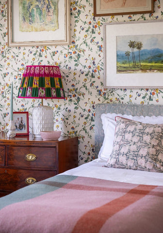 A vibrant patterned lampshade with bold pink green and yellow stripes on a textured white ceramic base with cushion cover