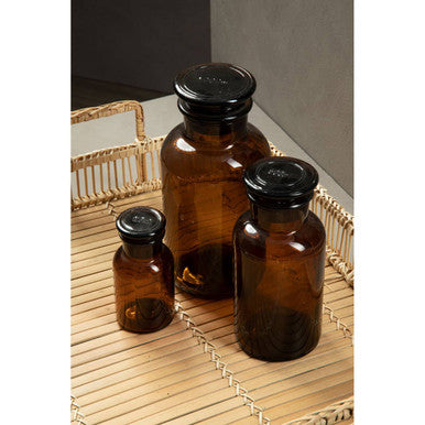 Set of three amber glass reagent bottles with black glass screw-top lids on a woven bamboo tray