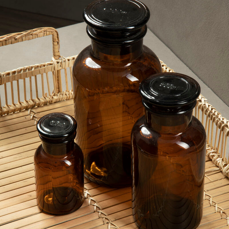 Three amber black glass reagent bottles with black screw-top lids and subtle vertical ridges in varying sizes