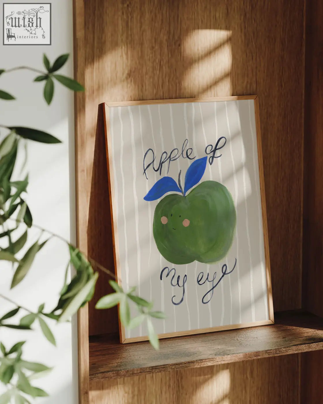 A framed apple of my eye food art print featuring a hand painted green apple with blue leaves and rosy cheeks