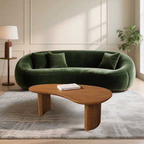 Deep emerald green velvet sectional sofa with plush rounded contours and matching pillows near aragon curved coffee table
