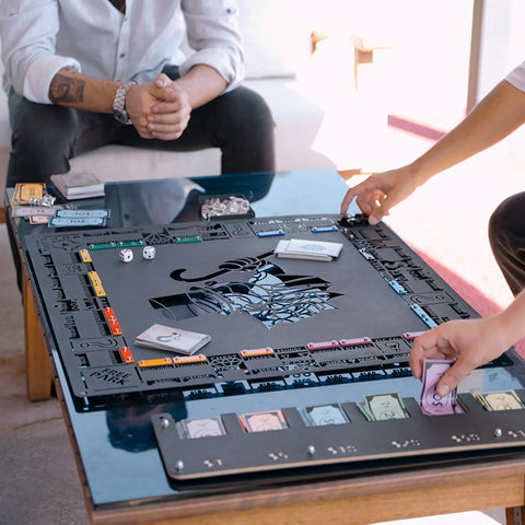 Black metal monopoly board with a stylized cat design and colorful property spaces featuring community chest cards on a flat surface for all age ranges