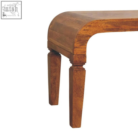 A warm-toned arcus coffee table made of oak solid mango wood with a curved top and turned legs for your living room