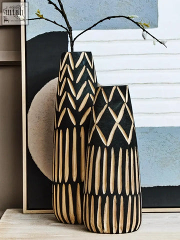 Two tall black and beige small engraved wooden vases with geometric patterns and a modern design