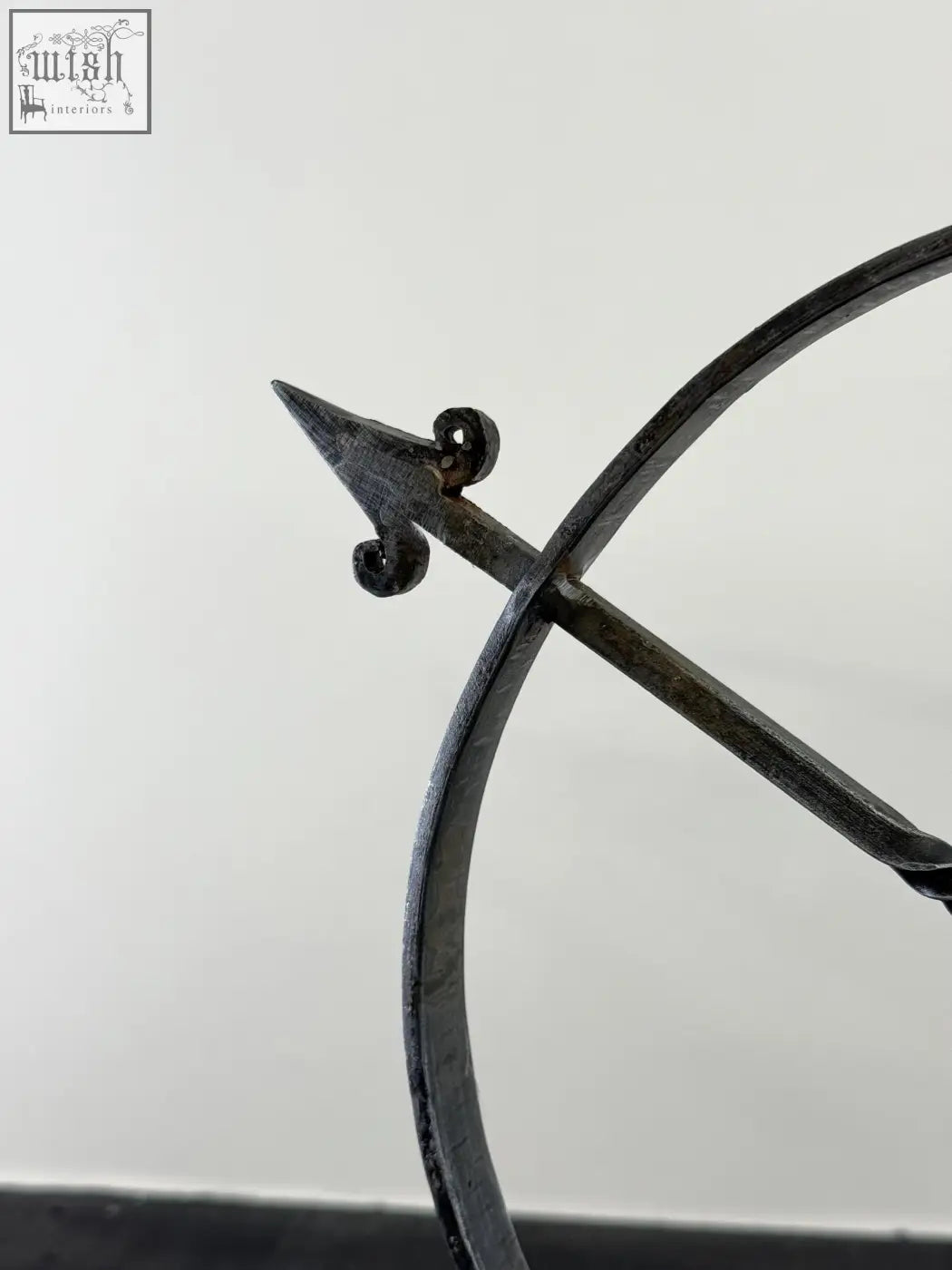 Dark solid iron armillary arrow sculpture with ornate scrollwork and hammer marks in wrought iron archer sculpture style