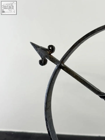 Dark solid iron armillary arrow sculpture with ornate scrollwork and hammer marks in wrought iron archer sculpture style