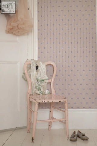 A delicate pink painted wooden chair with distressed finish and ornate curved backrest in arrows of love archive print wallpaper