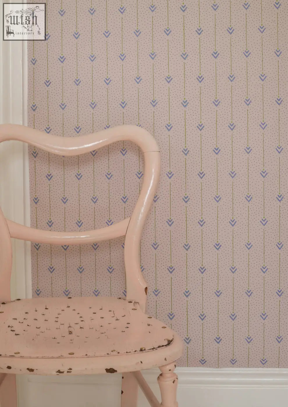 A vintage-style chair with a soft pink painted finish and ornate wood frame featured with arrows of love archive print wallpaper