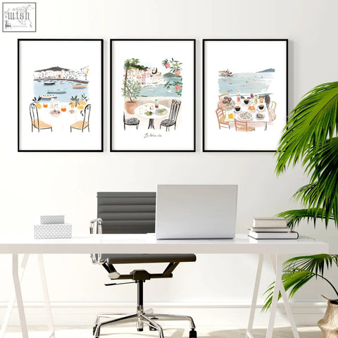 Three framed watercolor art prints of mediterranean coastal dining scenes hanging above a white office desk