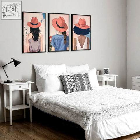 Three framed canvas prints of boho women wall art wearing coral hats hang above the bed as bedroom wall art