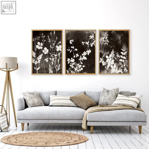 Three framed black and white botanical prints with delicate floral silhouettes in light wood frames for living room wall
