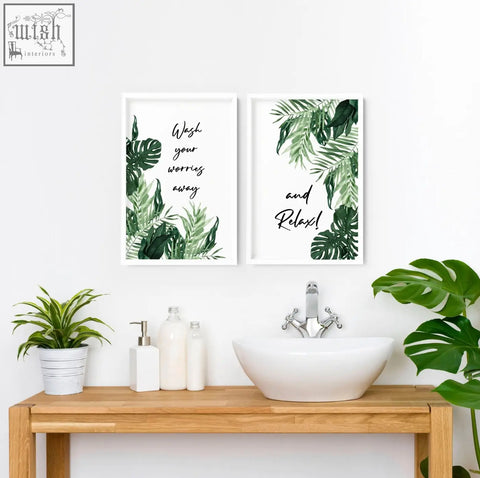 Two framed wall art prints with green leaf illustrations and black cursive text above a bathroom sink