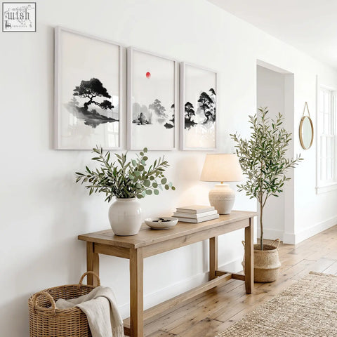 White ceramic vase holding green eucalyptus branches next to a black white red sun zen art landscape painting set of 3