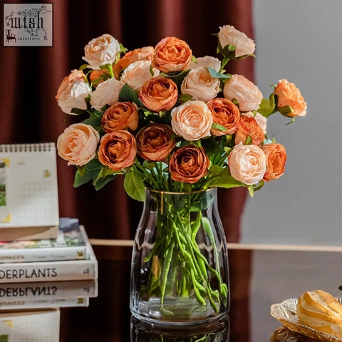 A clear glass vase with a gold rim holding peach and orange artificial roses for european entry lux rose living room decor