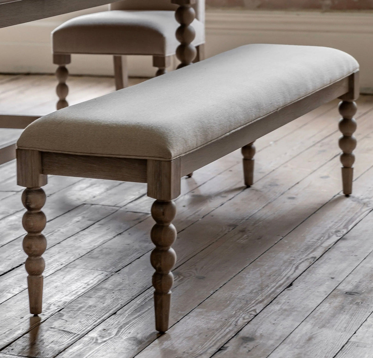 Artisan dining bench seat with light gray upholstered cushion and turned wooden legs in a rustic finish