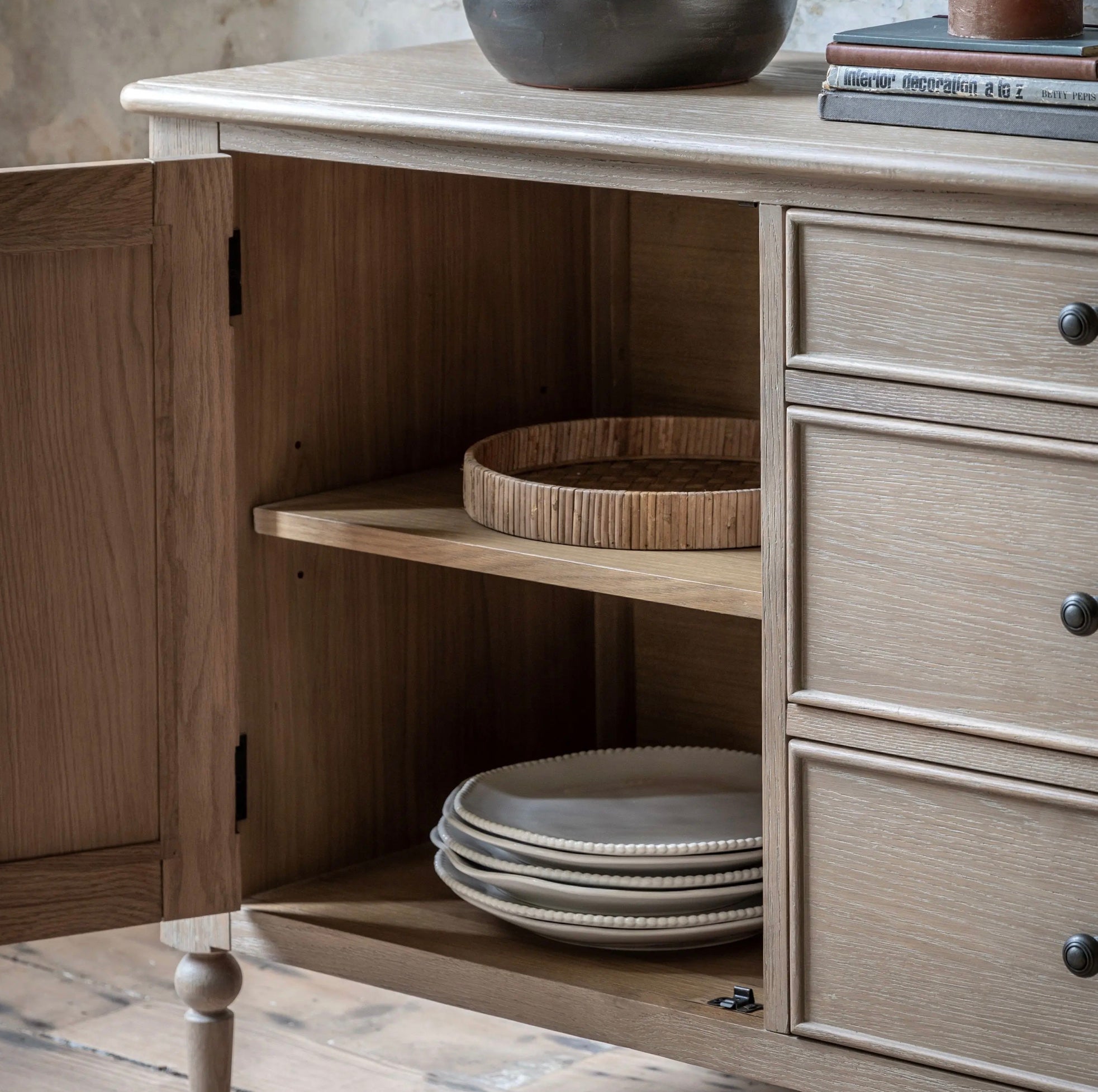 Light gray distressed wood artisan sideboard w457 x d350 with round woven bamboo tray and stacked beige plates inside
