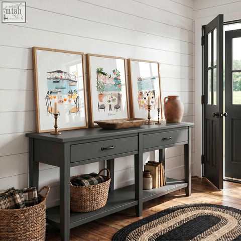 Dark gray console table with rustic wooden top black metal handles and open shelving shown with mediterranean coastal wall art prints set of three