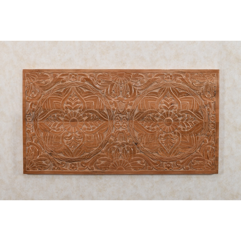 A rectangular light brown mango wood wall art piece with carved floral and geometric patterns for bedframe decor