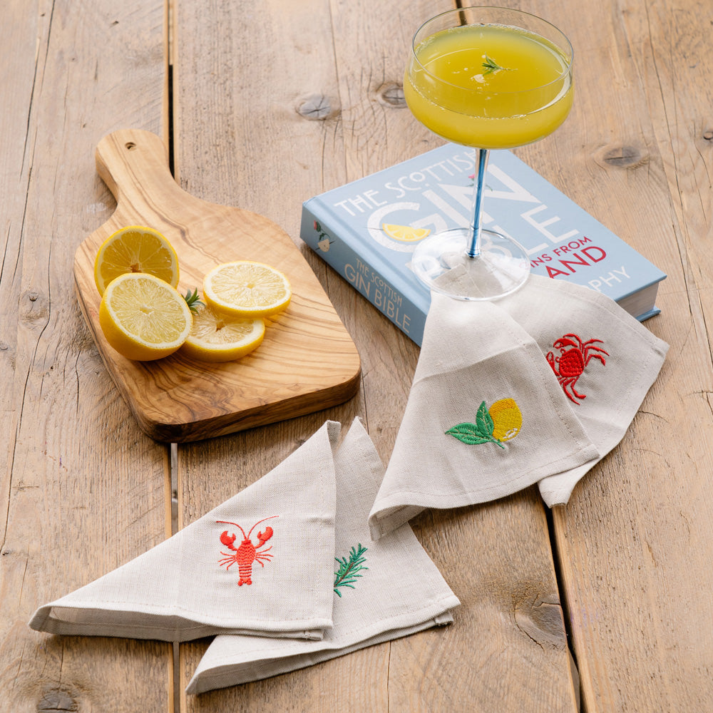 White linen cocktail napkins with embroidered red lobster green sprig and yellow lemon designs for coastal style