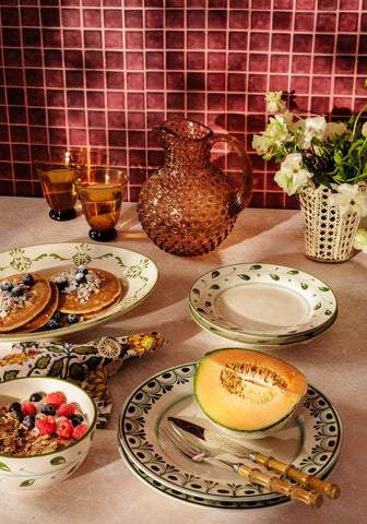 A textured amber glass pitcher with a bulbous body and handle next to a green iraca woven napkin ring