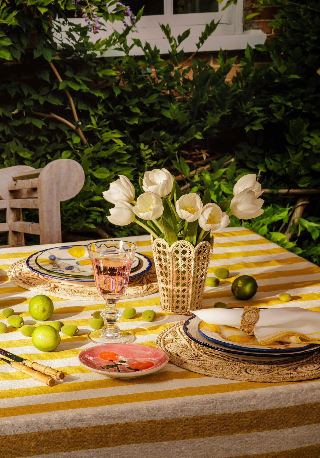 A cream-colored woven vase with white tulips next to a yellow atlántico iraca leaf napkin ring