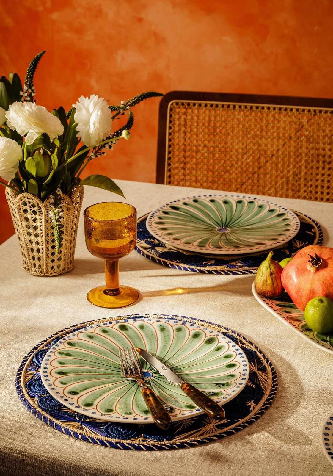 Green peacock-feather patterned ceramic dinner plate with blue and white border on atlántico iraca woven placemat blue