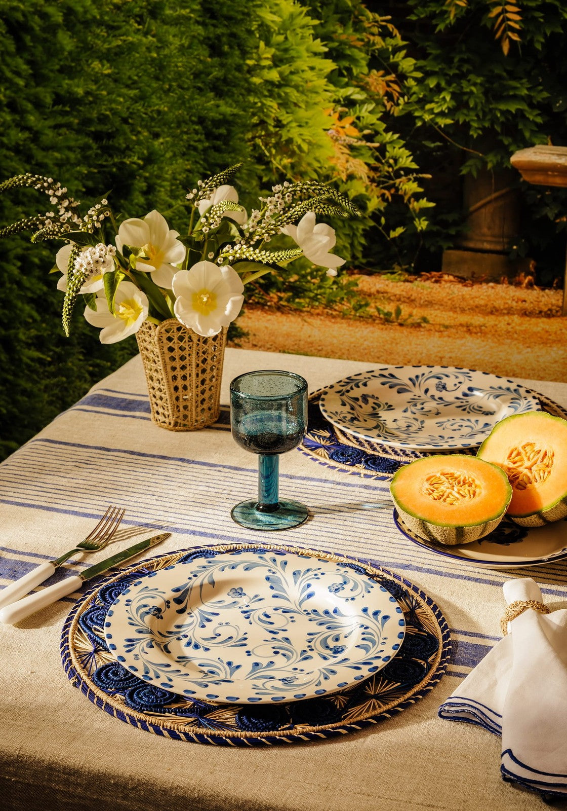 Blue and white patterned ceramic dinnerware set with intricate floral designs on atlántico iraca woven placemat blue