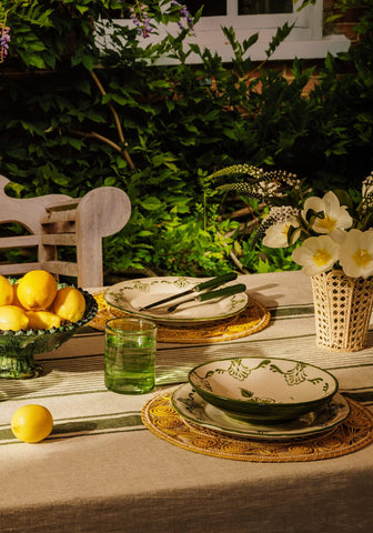 Green and white ceramic dinnerware with floral patterns on yellow atlántico iraca woven placemats