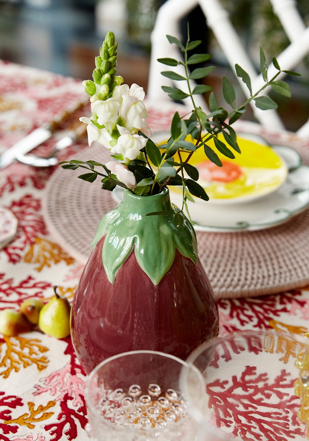 Aubergine bud vase is a deep red glossy ceramic strawberry shape with green leaves holding white flowers