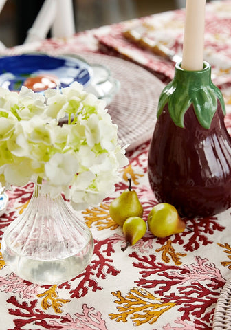 A glossy dark purple ceramic aubergine dream candle holder shaped like an eggplant with green leaves holding a white candle