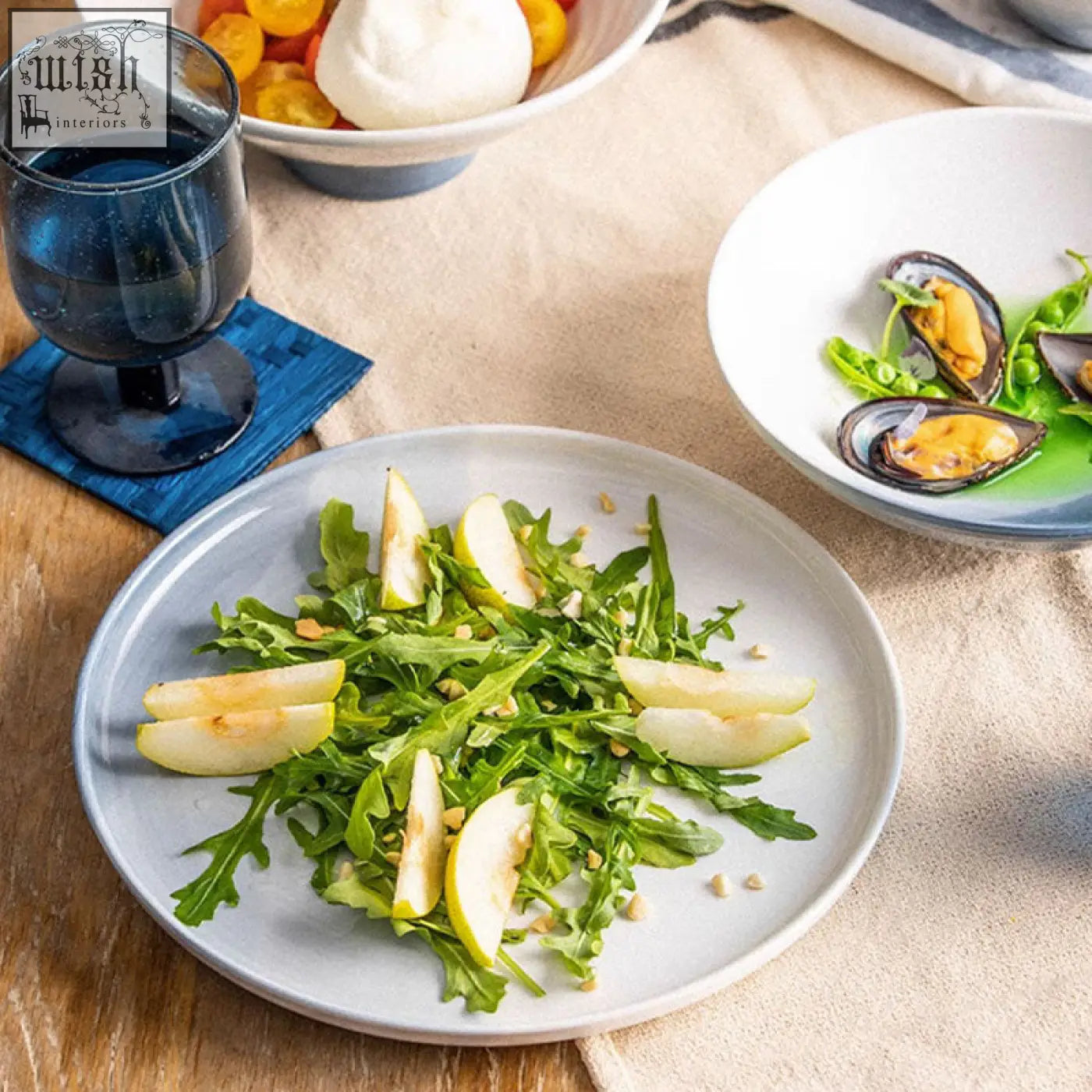 A light gray ceramic plate from the aurora dinner set holding fresh arugula salad with sliced apples and toasted nuts