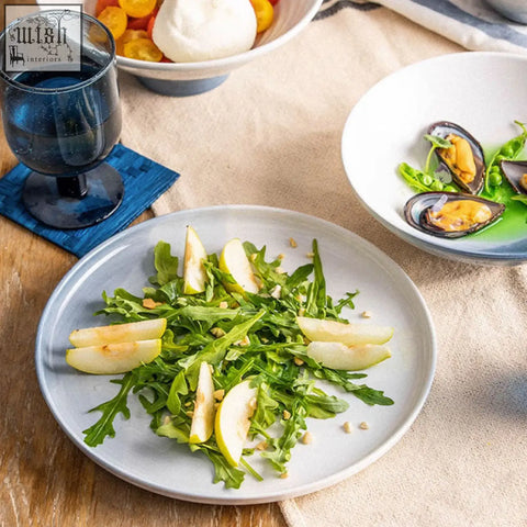 A light gray ceramic plate from the aurora dinner set holding fresh arugula salad with sliced apples and toasted nuts