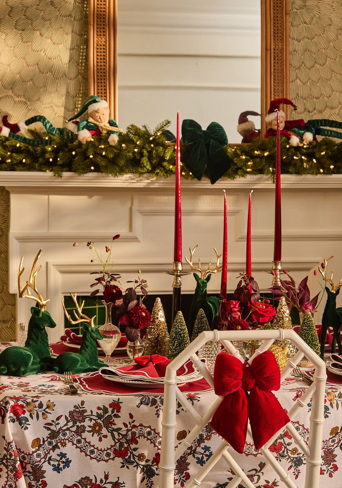 A plush red velvet bow tied on the back of a white bamboo chair with red slender taper candles nearby