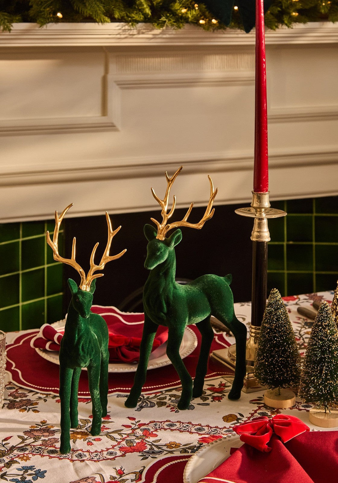 Two green velvet deer figurines with gold antlers on a festive table with aurora medium slender taper candles red