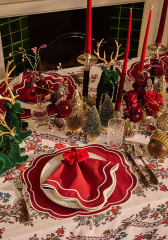 A red velvet napkin with a white scalloped edge and bow placed next to red slender taper candles