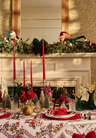 Aurora medium slender taper candles in red with red velvet reindeer figurines featuring gold antlers nearby