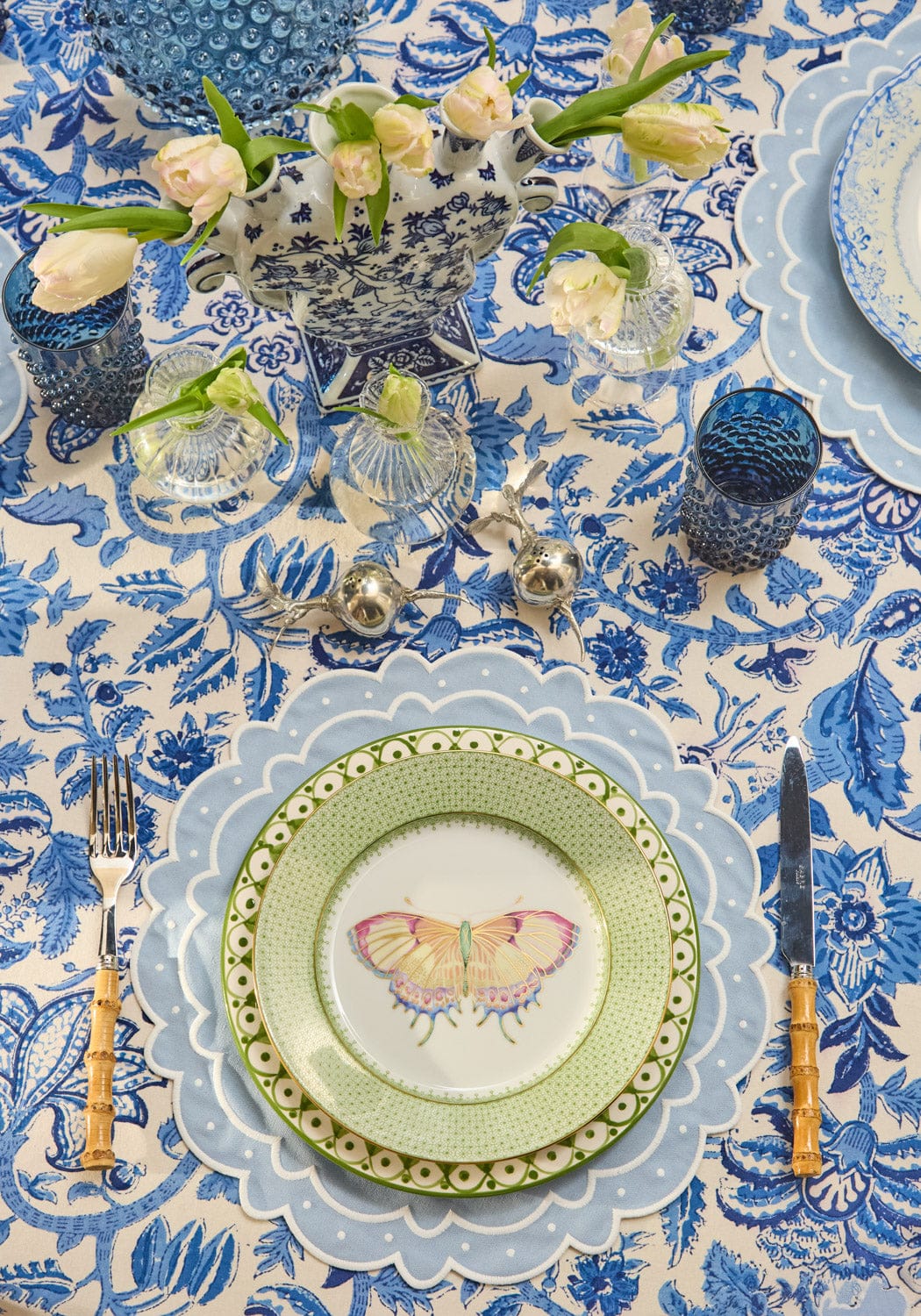 A delicate green plate with a scalloped edge and butterfly design shown with the aurora set of 4 light blue placemats