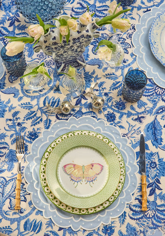 A delicate green plate with a scalloped edge and butterfly design shown with the aurora set of 4 light blue placemats