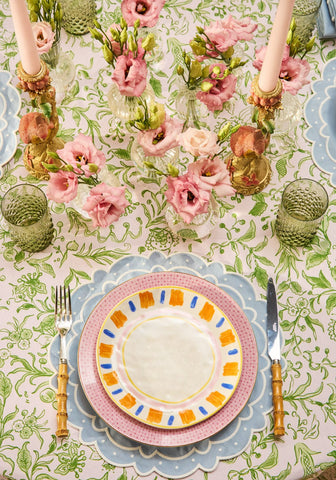 A vibrant pink and blue patterned ceramic plate on a light blue aurora set of 4 placemats with scalloped edges
