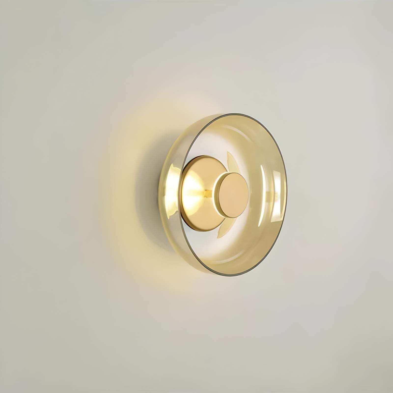 Aurora wall lamp with a modern circular design featuring translucent amber glass and polished gold metal accents