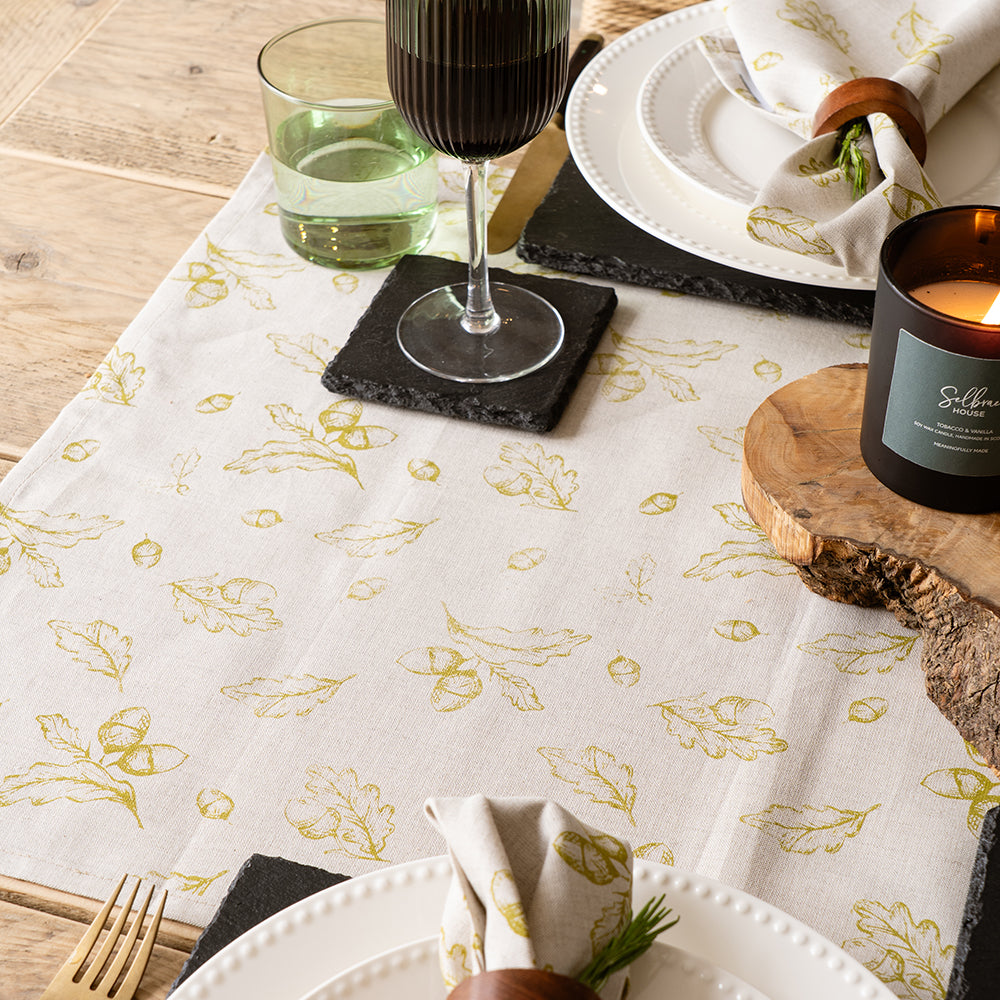 Cream-colored linen table runner with gold leaf and acorn pattern and subtle textured weave for autumn decor